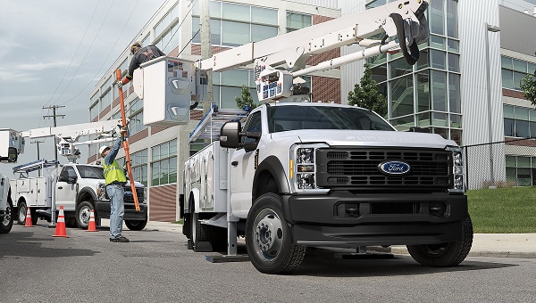 Ford Super Duty Chasis blanca con brazo elevador y cesta trabajando en la calle, con operarios.